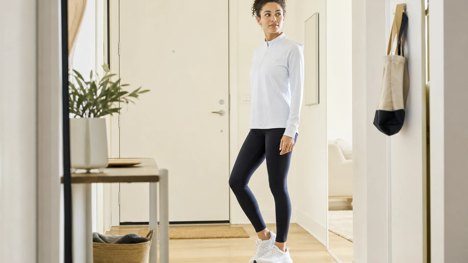 A woman in athletic clothes standing in a bright hallway near a door
